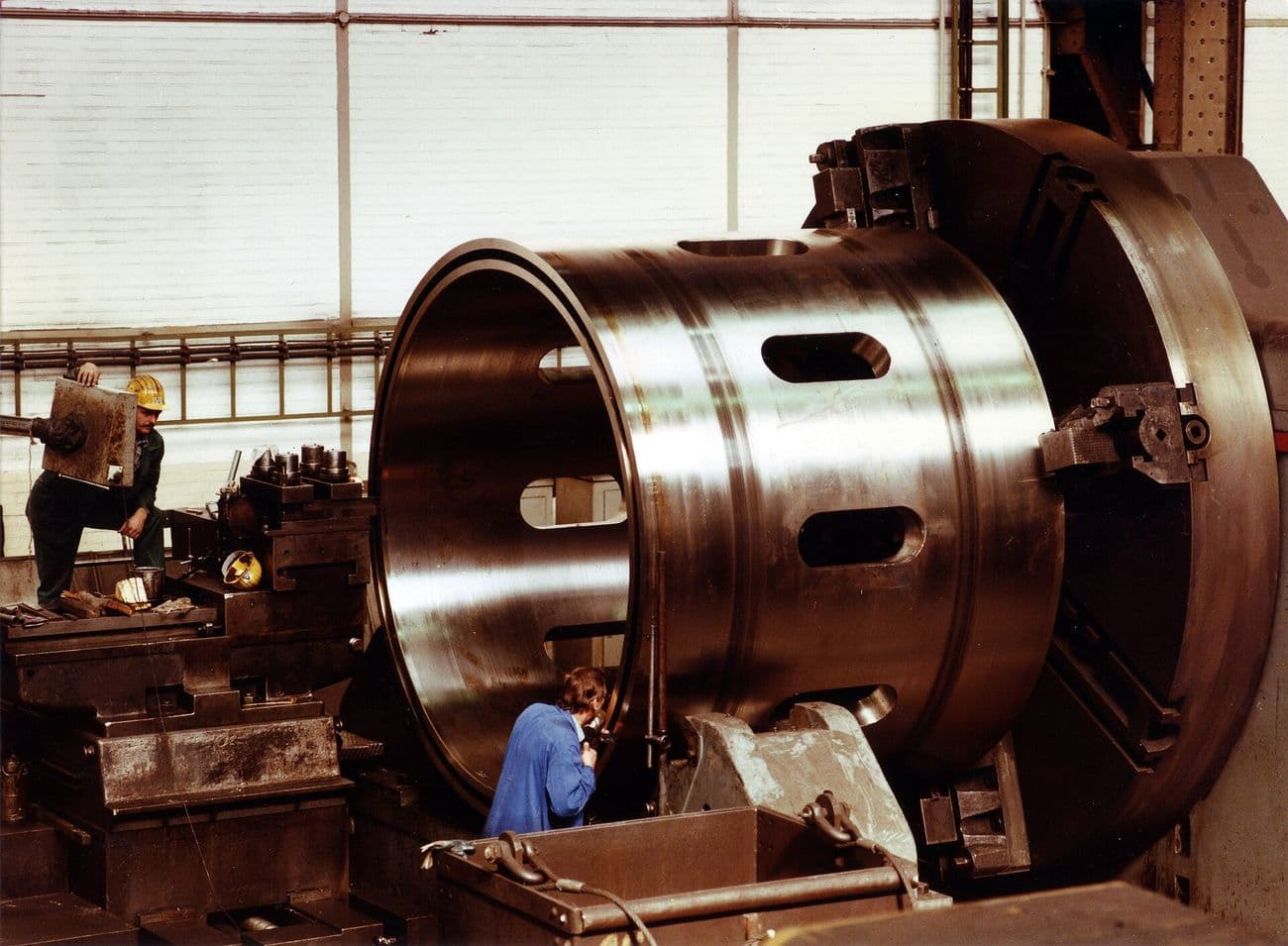 A large steel ring being machined on a heavy lathe in a workshop.