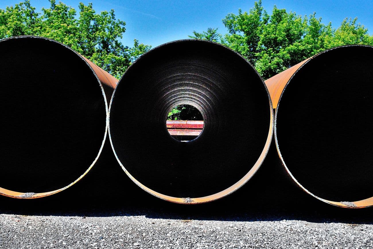Three large-diameter steel tubes lying side by side on gravel.